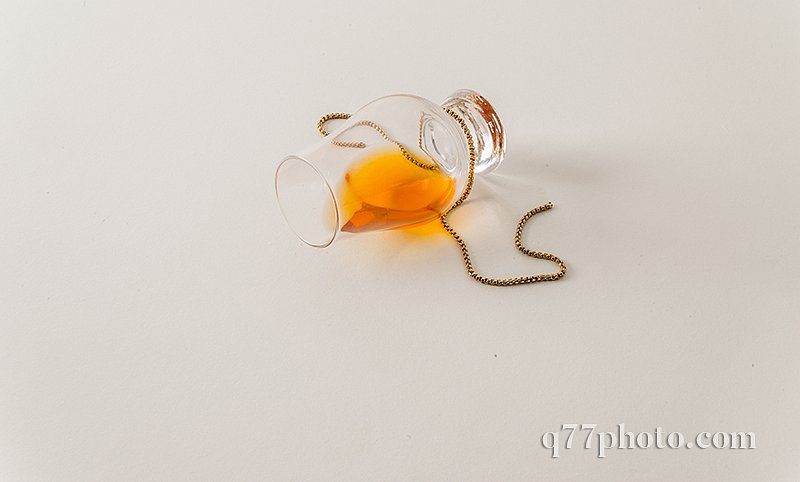 Overturned single malt whiskey glass, on white, with gold chain